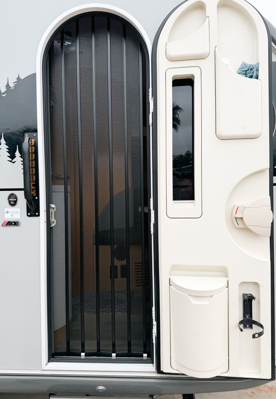 Black folding screen fitted to the arched door of a teardrop RV trailer