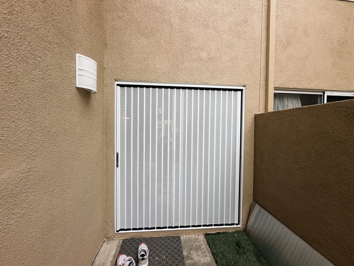 White folding screen on a side-yard door between stucco walls