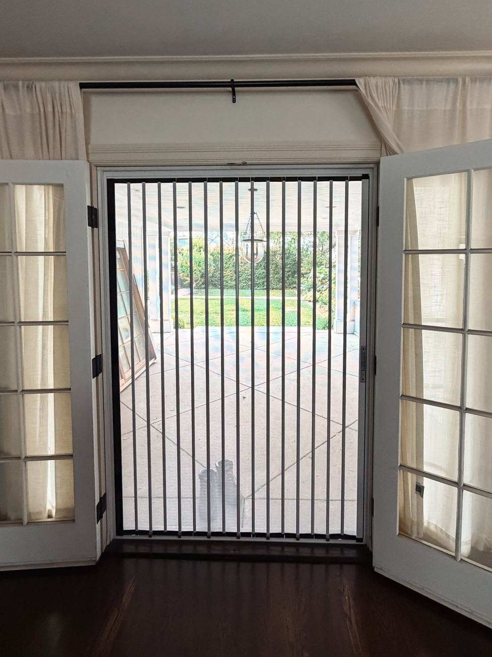 View from inside through a white folding screen between two open French doors to a covered patio