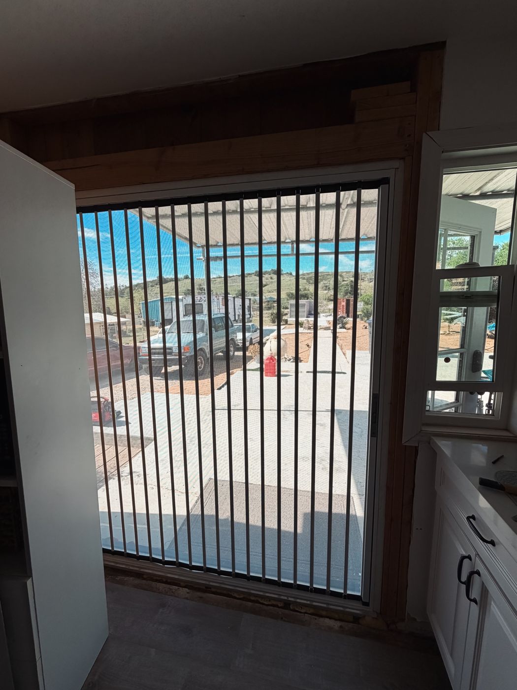 View from inside through a folding screen to a sunny driveway